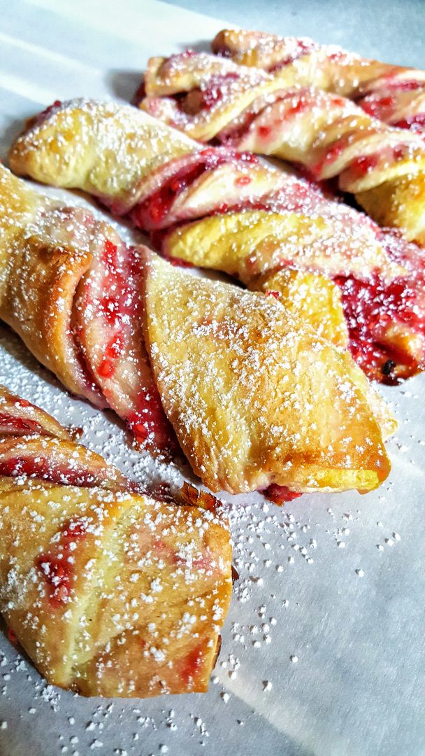 raspberry twist pastries with light powdered sugar laying on parchment paper