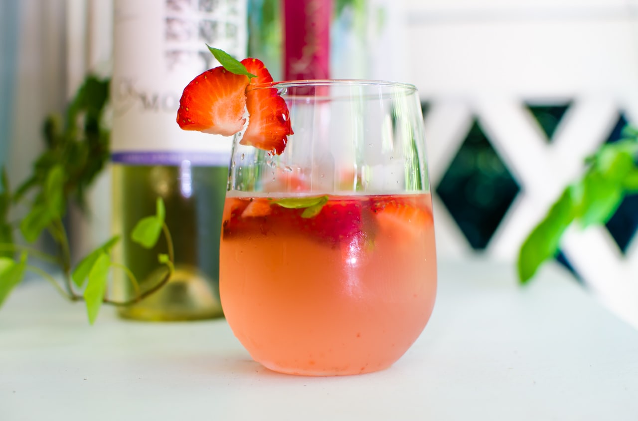 cocktail with strawberry on rim in front of wine bottle