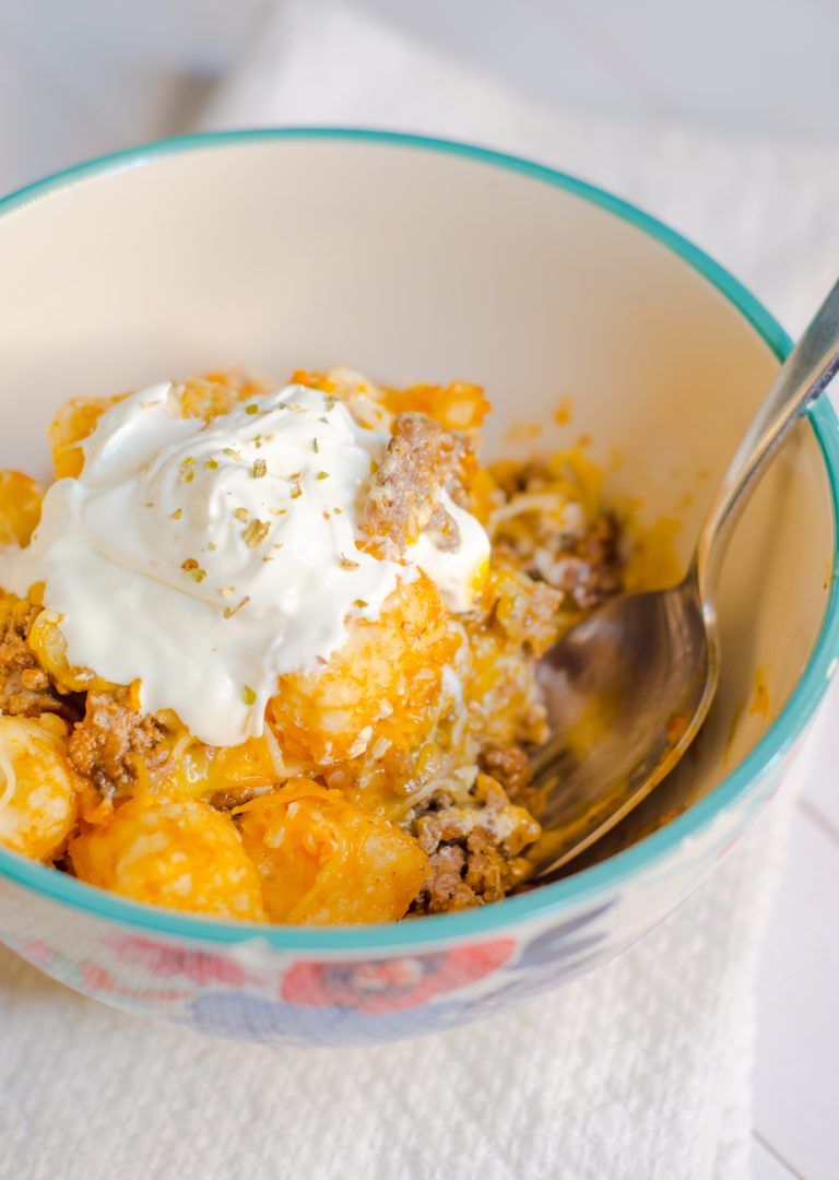tater tot casserole in bowl with spoon and sour cream