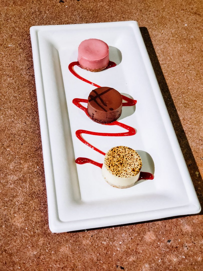 Plate with trio of cheesecake samples of raspberry, New York-style, and chocolate.