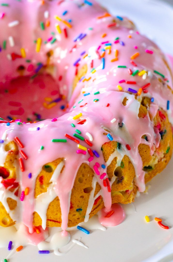 bundt cake with pink and white glaze and sprinkles over the top