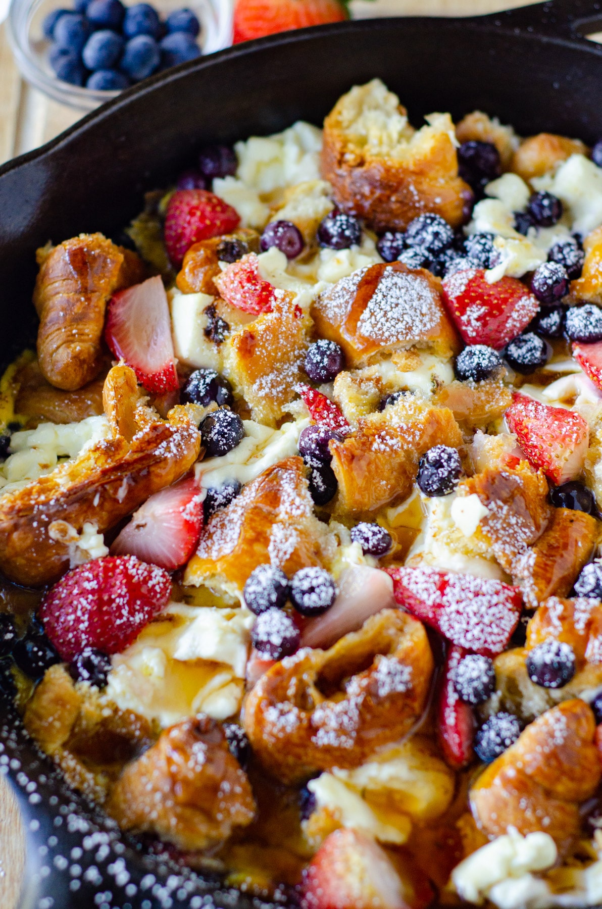 Croissant Breakfast Casserole served with strawberries and blueberries in a cast iron skillet.