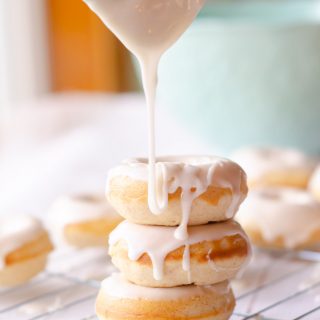 baked donuts with white glaze being poured over the top