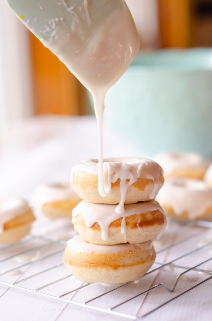 baked donuts with white glaze being poured over the top